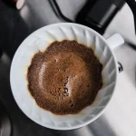 V60 드리퍼에서 갓 부은 물에 원두가 부풀어 오르는 블룸(blooming) 장면 — 탈가스 중 방출되는 CO2